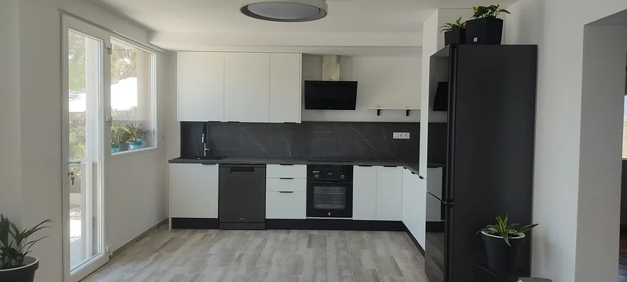 Weiße L-Küche mit Arbeitsplatte und Nischenrückwand in dunkelgrauer Marmoroptik und schwarzen Elektrogeräten
